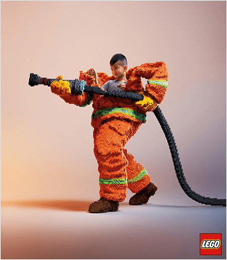Bu, LEGO'lardan yapılmış bir itfaiyeci üniforması içinde genç bir Asyalı çocuğu gösteren bir LEGO reklamından bir fotoğraf. Üniforma, ceket ve pantolonun manşetlerinin etrafında neon yeşili bir şeritle turuncu renktedir. İtfaiyeci bir ayağı geride duruyor ve yine legolardan yapılmış bir yangın hortumu tutuyor. Çocuğun kafası, olduğundan çok daha büyük olan ve omuzlarının etrafında duran üniformanın üstünden görünüyor. Fotoğraf, sade nötr bir arka plana karşı çekildi. LEGO logosu sağ altta kırmızı bir kutu içinde görünür. Talia Wolf, LEGO'nun reklamlarda duygu kullanan bir markanın harika bir örneği olduğunu söylüyor.